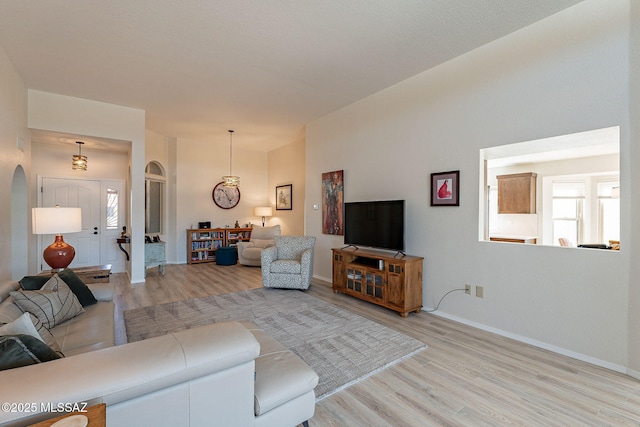 living area featuring arched walkways, light wood-type flooring, and baseboards