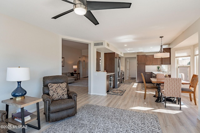 living area with light wood finished floors, visible vents, a ceiling fan, and baseboards