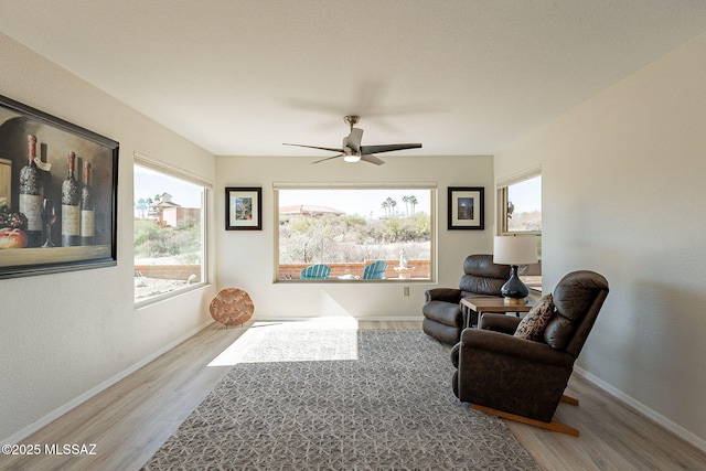 living area featuring wood finished floors, baseboards, and ceiling fan