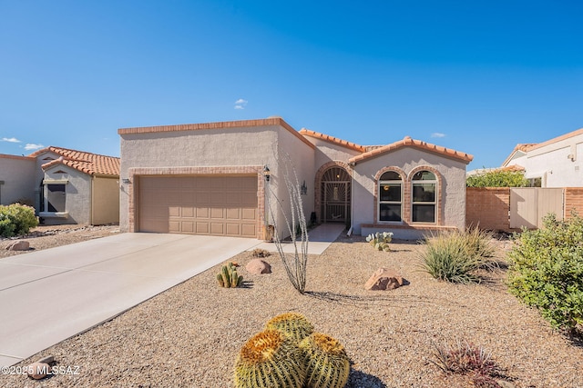 mediterranean / spanish-style house with fence, an attached garage, stucco siding, concrete driveway, and a tiled roof