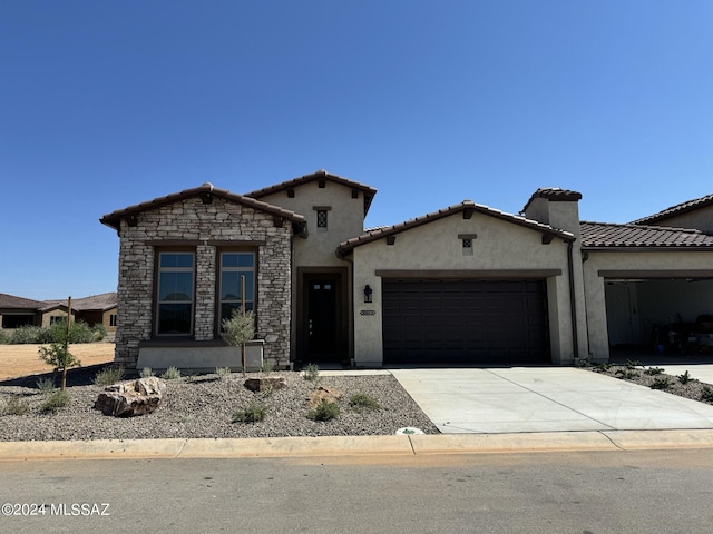 mediterranean / spanish-style house featuring stucco siding, driveway, a tile roof, stone siding, and an attached garage