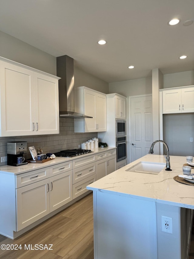 kitchen with a sink, light stone counters, appliances with stainless steel finishes, wall chimney exhaust hood, and decorative backsplash