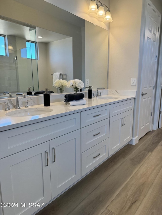 full bath featuring a tile shower, double vanity, wood finished floors, and a sink