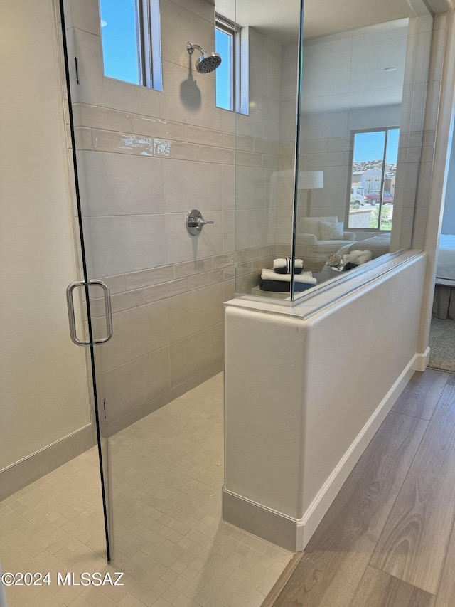 ensuite bathroom featuring a wealth of natural light, wood finished floors, a tile shower, and ensuite bathroom