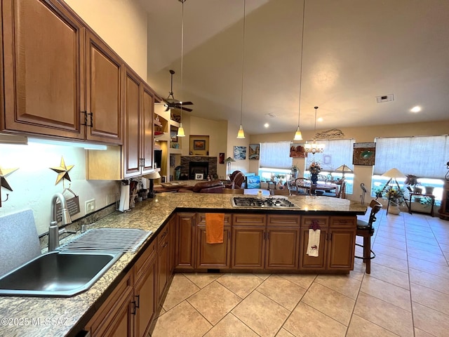 kitchen with ceiling fan, stainless steel gas cooktop, a peninsula, a fireplace, and a sink