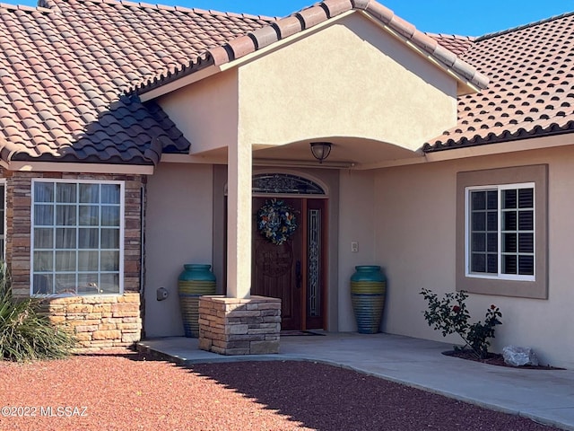 doorway to property featuring stucco siding, stone siding, and a tiled roof