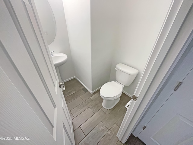 half bath with toilet, baseboards, and wood tiled floor