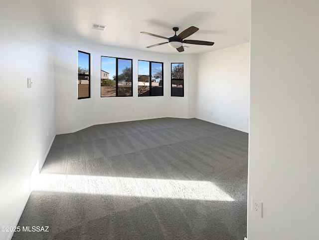 empty room with visible vents, dark carpet, baseboards, and ceiling fan