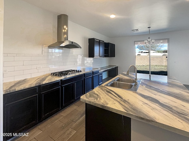 kitchen with dark cabinetry, wood finished floors, stainless steel gas cooktop, island exhaust hood, and a sink