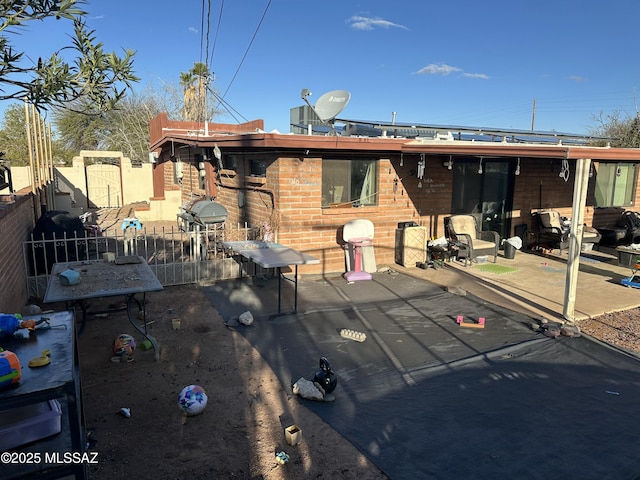 rear view of house featuring a patio area, brick siding, and fence