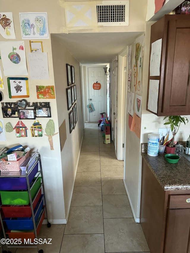 hallway with light tile patterned floors, visible vents, and baseboards