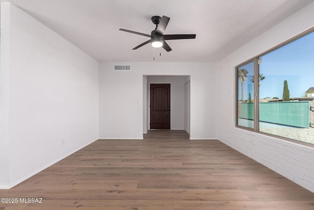 unfurnished room featuring a ceiling fan, wood finished floors, visible vents, and brick wall