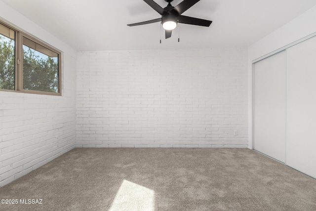 unfurnished bedroom with a closet, brick wall, ceiling fan, and carpet floors