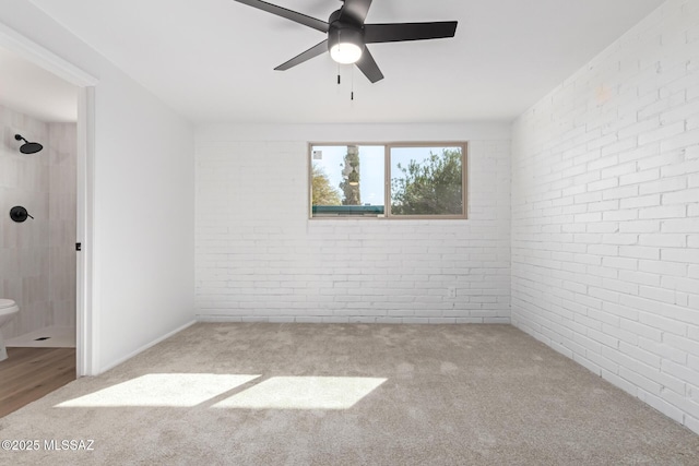 carpeted spare room featuring brick wall and a ceiling fan