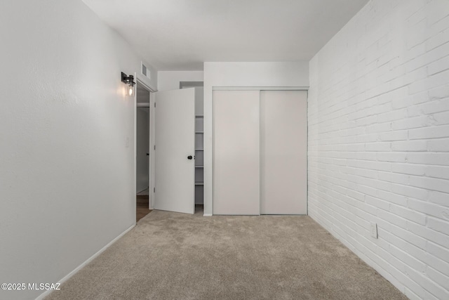 unfurnished bedroom featuring visible vents, a closet, brick wall, and carpet flooring