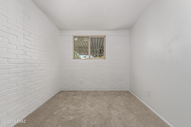 carpeted spare room featuring brick wall