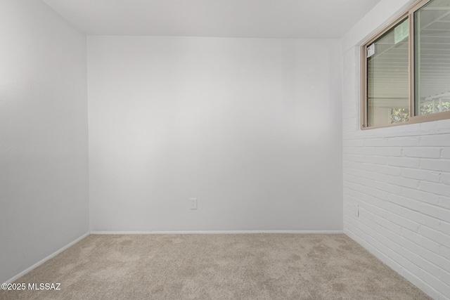 unfurnished room featuring brick wall, baseboards, and carpet