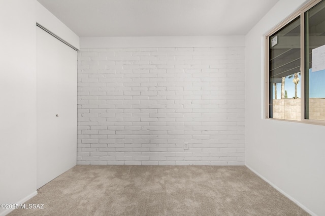 unfurnished room featuring brick wall and carpet floors