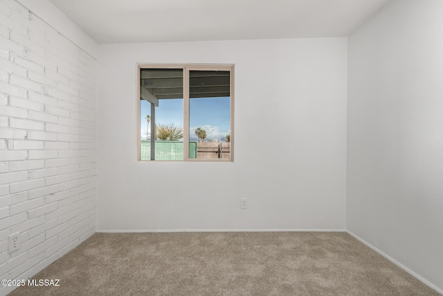 carpeted spare room with brick wall and baseboards