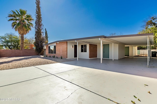 view of front of house with brick siding, an attached carport, driveway, and fence