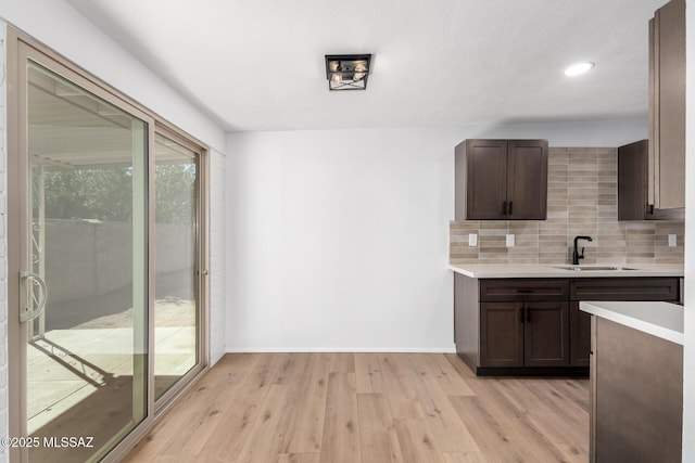 kitchen with tasteful backsplash, dark brown cabinetry, light countertops, light wood-style floors, and a sink