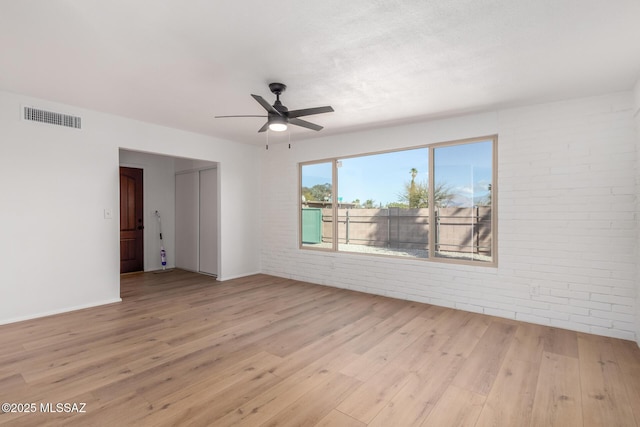 empty room with visible vents, ceiling fan, brick wall, and light wood-style floors