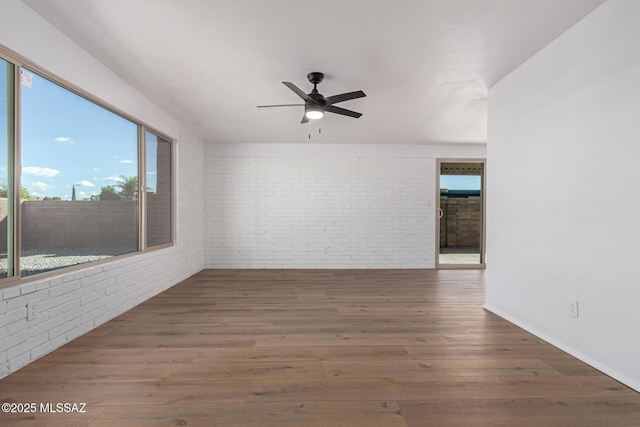 empty room with ceiling fan, wood finished floors, and brick wall