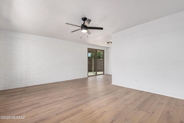 spare room featuring wood finished floors, brick wall, and ceiling fan