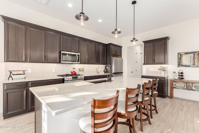 kitchen featuring dark brown cabinetry, a sink, light stone countertops, hanging light fixtures, and stainless steel appliances
