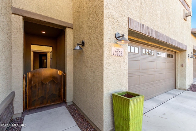 property entrance with driveway, stucco siding, and an attached garage