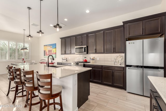 kitchen with tasteful backsplash, dark brown cabinetry, appliances with stainless steel finishes, a sink, and a breakfast bar area