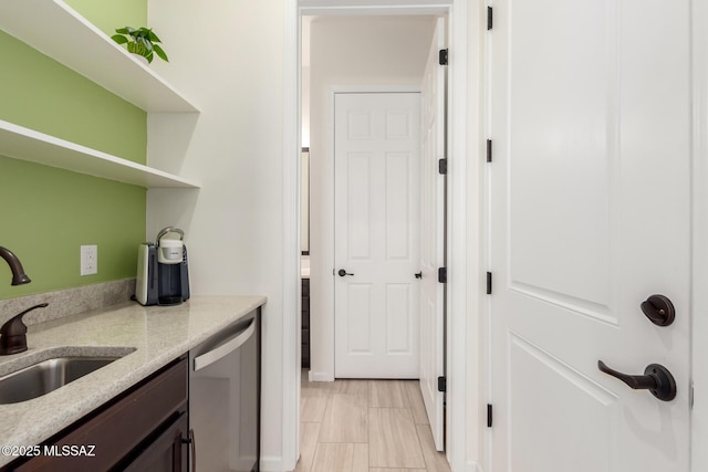 kitchen featuring open shelves, a sink, dishwasher, light stone countertops, and dark brown cabinetry