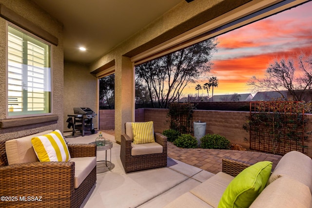 patio terrace at dusk featuring an outdoor living space, fence, and grilling area