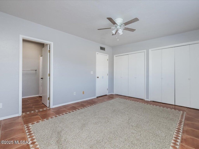 unfurnished bedroom featuring tile patterned floors, baseboards, visible vents, two closets, and ensuite bath