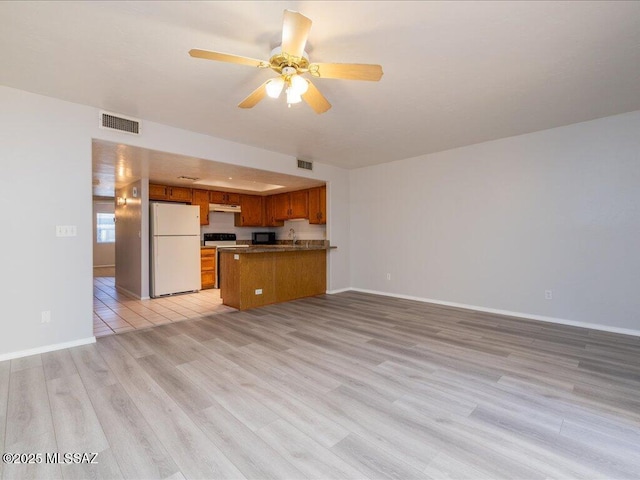 kitchen with brown cabinetry, visible vents, freestanding refrigerator, under cabinet range hood, and open floor plan