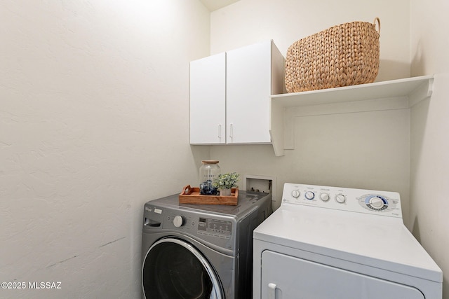 laundry area with cabinet space, washer and dryer, and a textured wall