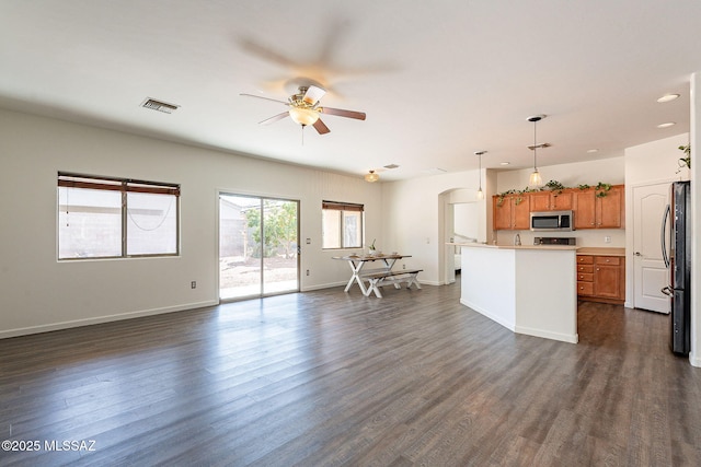 kitchen with stainless steel microwave, visible vents, brown cabinetry, open floor plan, and arched walkways