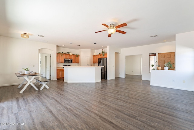 unfurnished living room featuring visible vents, arched walkways, dark wood-style floors, and a ceiling fan