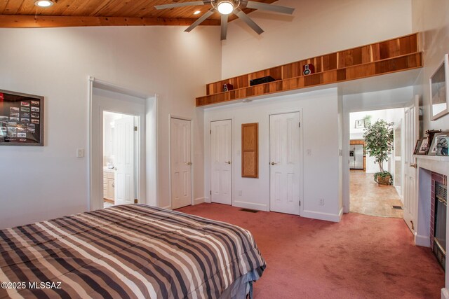 carpeted bedroom featuring two closets, baseboards, wooden ceiling, a glass covered fireplace, and high vaulted ceiling