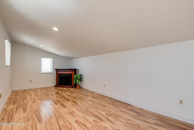 unfurnished living room featuring baseboards, light wood-style floors, a fireplace with raised hearth, and vaulted ceiling