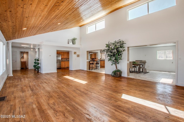 unfurnished living room featuring visible vents, high vaulted ceiling, wood finished floors, wooden ceiling, and baseboards