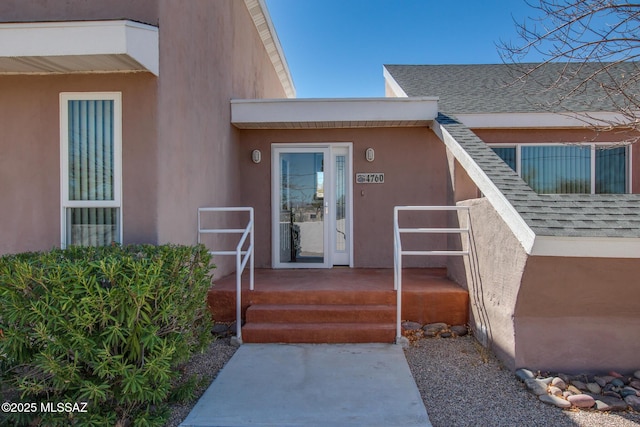 view of exterior entry with stucco siding and a shingled roof