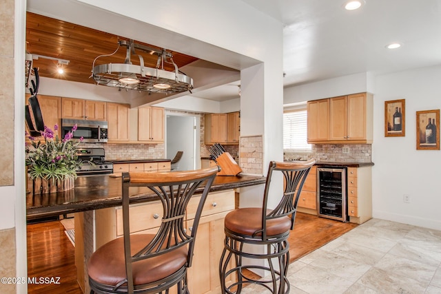 kitchen with light brown cabinets, a kitchen breakfast bar, dark countertops, stainless steel appliances, and wine cooler