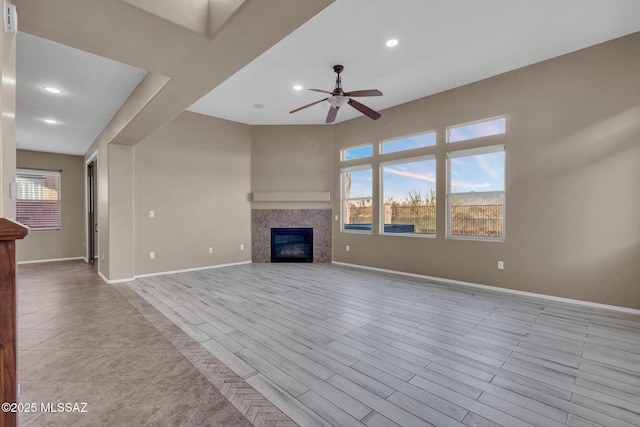 unfurnished living room with a wealth of natural light, baseboards, ceiling fan, and a tile fireplace