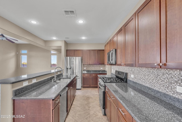 kitchen featuring visible vents, dark stone counters, a sink, ceiling fan, and stainless steel appliances