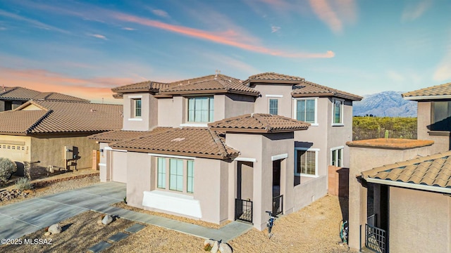 mediterranean / spanish home featuring concrete driveway, a tiled roof, a mountain view, and stucco siding