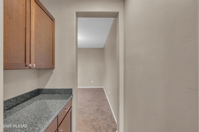 kitchen with brown cabinetry, dark stone counters, and baseboards