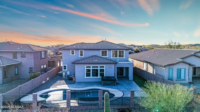 back of property at dusk featuring stucco siding, a tiled roof, a fenced backyard, and a patio