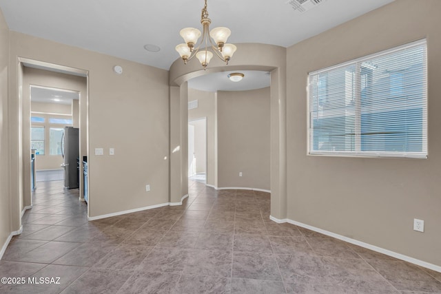 tiled spare room featuring baseboards, visible vents, arched walkways, and an inviting chandelier