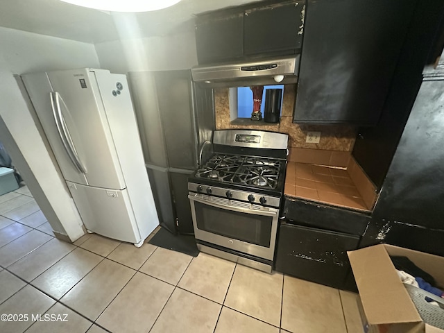 kitchen with stainless steel range with gas cooktop, under cabinet range hood, decorative backsplash, freestanding refrigerator, and light tile patterned flooring